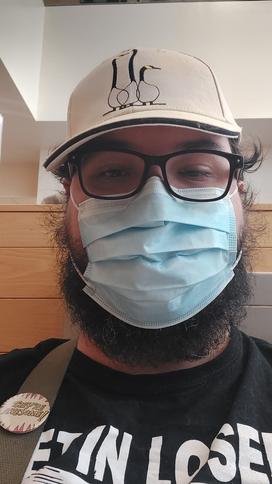 A man with short hair and bushy facial hair sits in a hospital waiting room, wearing a blue surgical mask